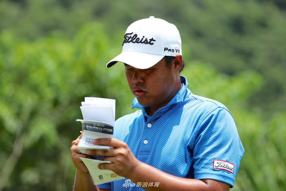 中国球员张进在果岭上全神贯注地观察推杆线路，眼神坚毅，背后是典型的桂林山景。