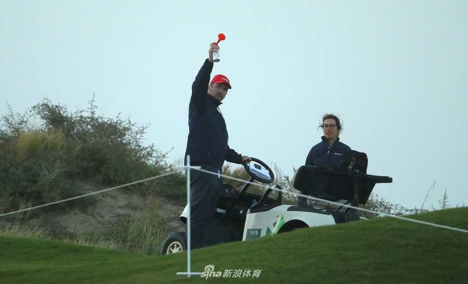 艾尔莫吉高尔夫球场全景，碧蓝海水环抱下的金黄球道与果岭，与远处朦胧的山峦构成壮丽画卷，挑战即将在此展开。