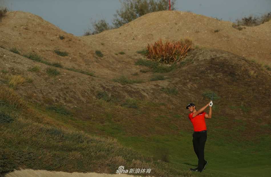 宽阔的球道在沙丘间蜿蜒延伸，远处是现代化城市天际线，自然荒凉之美与人类绿洲创造形成鲜明对比。