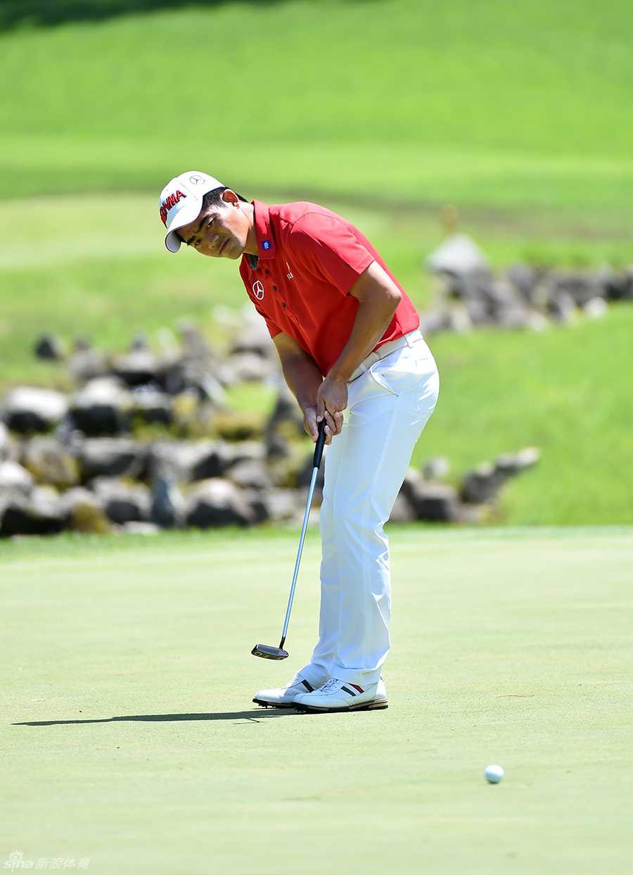 梁文冲站在果岭边，双手扶膝，身体微微前倾，正从低角度极其专注地观察推杆线路的起伏与草纹走向。